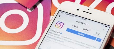 The image shows a smartphone displaying an Instagram feed with a post featuring a collection of colorful stickers and a white card with the Instagram logo, placed next to the phone.