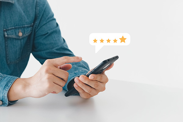 A person's hand holding a smartphone with a speech bubble containing a star rating, suggesting customer feedback or satisfaction.