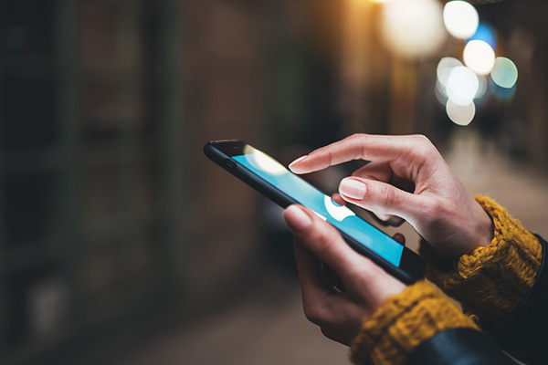 A person holding a smartphone with a lit screen, displaying content on a street at night.