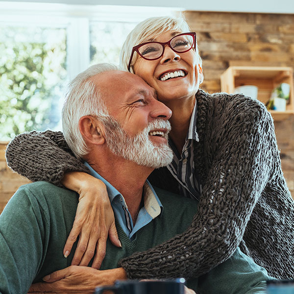 The image shows an older couple, a man and a woman, embracing each other warmly with smiles on their faces.