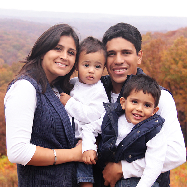 Family of four posing for a photograph in front of autumn foliage.
