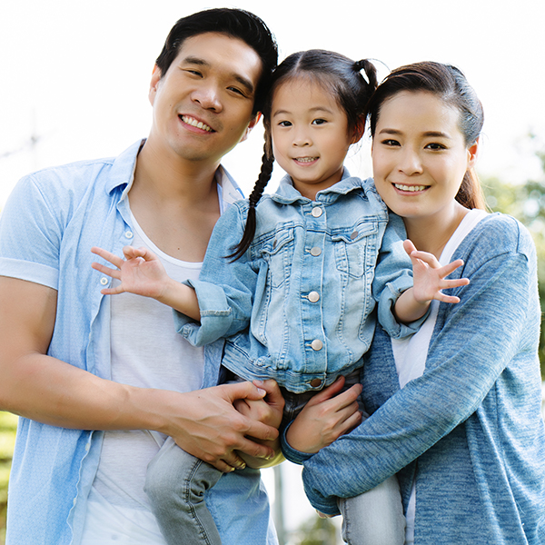 A family of three poses for a photo, with the father holding a young child and the mother standing behind them.