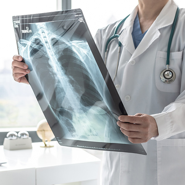 The image shows a medical professional holding up an X-ray of a human chest, viewed through a transparent overlay that appears to be a digital display.