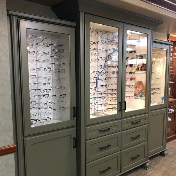 The image shows a large, green cabinet with glass doors displaying an assortment of eyeglasses.