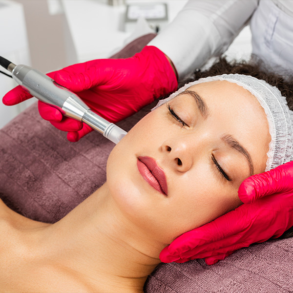 Woman receiving a cosmetic treatment, likely at a beauty salon, with a device being applied to her face by a professional.