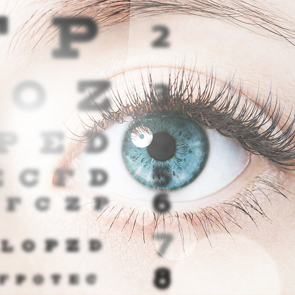 The image shows a close-up of an eye with blue irises, viewed through a magnifying glass or similar device, displaying an enlarged view of the eye's details, including eyelashes and pupil, against a blurred background.