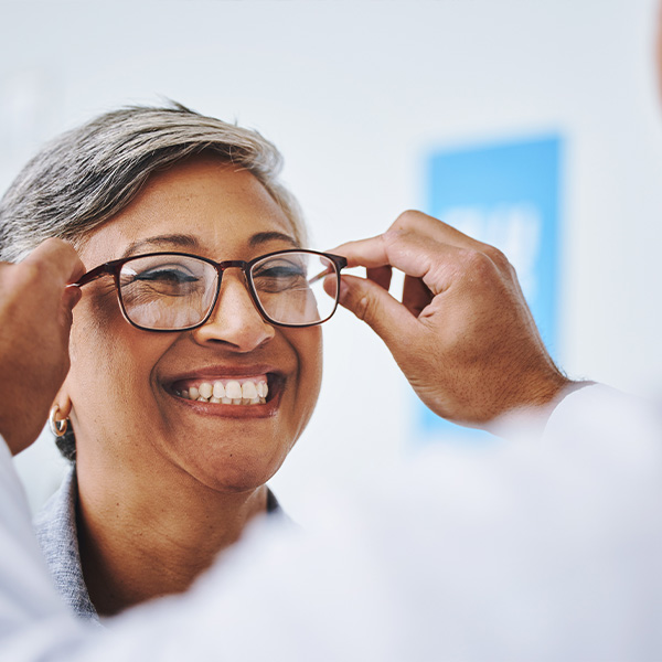An elderly woman with glasses and a smile, being adjusted by an optician in a professional setting.