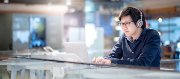 A person sitting at a desk with a laptop and headphones, working in an office environment.