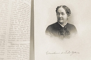 The image is a black and white photograph of a woman with short hair, wearing a dark dress with lace detailing. She is positioned in front of an open book, which has text on the page visible to us. Her expression appears contemplative, and she is looking slightly away from the camera.