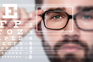 Close-up of a man with glasses and a beard, looking attentively at an eye chart.