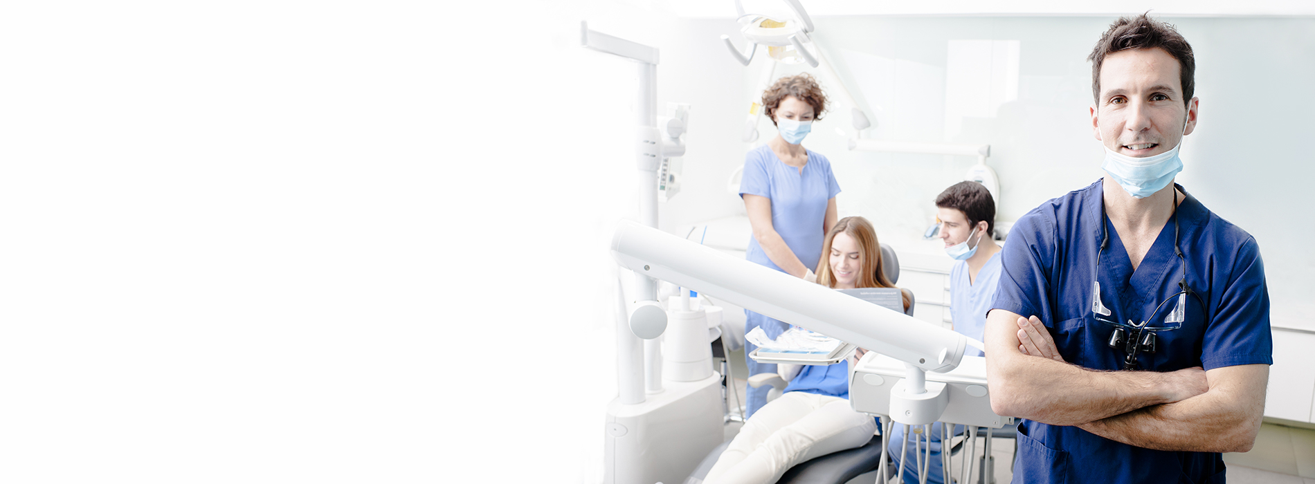 The image shows a dental office interior with a dentist standing in front of the camera, smiling at it.