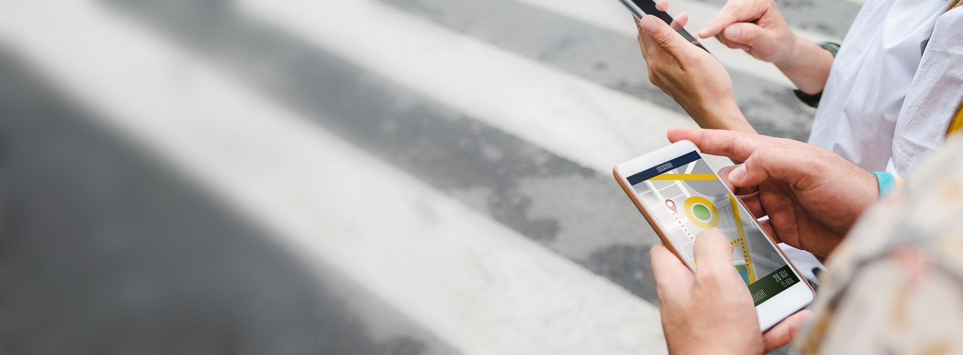 A person using a smartphone while standing on a sidewalk, with another individual partially visible in the background.