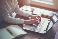 A woman sitting at a desk using a laptop, with books and a notebook nearby.