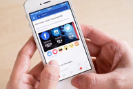 The image shows a hand holding a smartphone displaying a social media feed with various posts and icons.