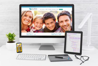 The image displays a computer monitor showing a website with a family photo, accompanied by a tablet and a smartphone on a desk.