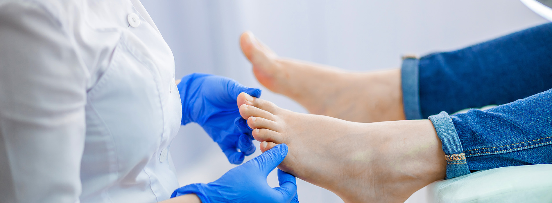 A healthcare professional wearing gloves and a white coat attends to a patient s foot, with the focus on the medical treatment being administered.