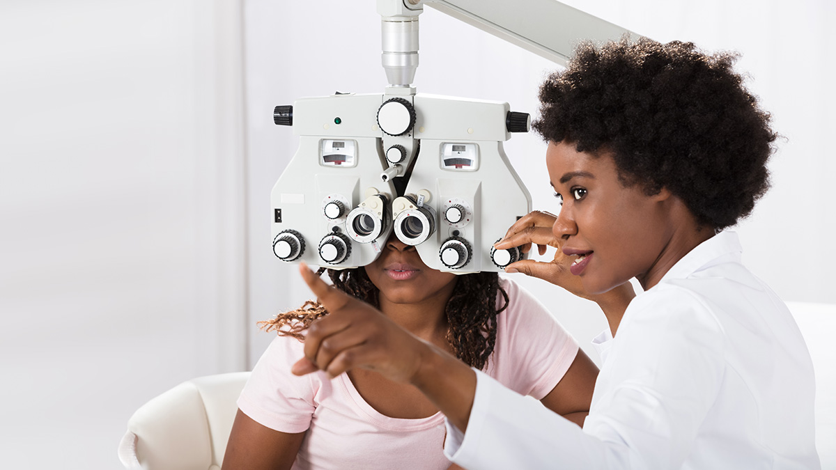An optometrist performing an eye examination on a seated patient.