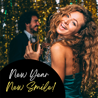 A woman in a green dress is holding a champagne flute, smiling and celebrating at a New Year's party with confetti in the background.