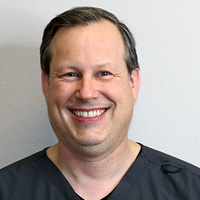 A man is smiling at the camera in a professional setting.