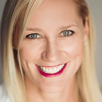 The image shows a woman with blonde hair, wearing red lipstick and a white top, smiling at the camera.