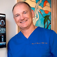 The image shows a man in a blue scrub suit, standing next to an ultrasound machine with a smiling expression.