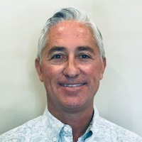 A man with short hair and a beard, wearing a patterned shirt, smiling at the camera.